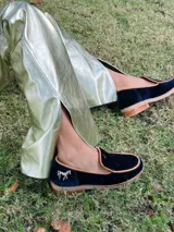 Mocasines de diseño clásico en terciopelo azul marino con ribete tostado y aplique metálico de caballo en el lateral del talón.