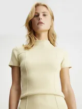 Sweater de punto canalé color crema, ajustado al cuerpo, con cuello mock y mangas cortas. Presenta costuras visibles que definen la silueta y un pequeño bolsillo decorativo en el pecho. Incluye una etiqueta con el logo 'CK' en el bajo.