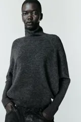 Jersey de punto liso color gris oscuro, con cuello subido y diseño de manga murciélago con sisa amplia que se ajusta hacia la muñeca.