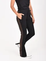 Pantalón negro con franja lateral marrón, cintura elástica con cordón ajustable, bolsillos laterales con cierre y cierres en los tobillos.
