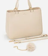 Cartera satchel mediana color beige, con cierre de cremallera, correa de mano y bretel largo desmontable. Incluye un llavero de pompón de piel sintética.