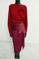 Falda midi de tiro medio confeccionada en tejido satinado con estampado de lunares. Presenta un diseño envolvente con detalle de volante lateral y cierre posterior con cremallera oculta.