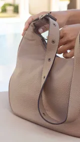 Cartera tipo hobo o media luna de cuero sintético negro, con textura granulada. Posee una correa ajustable para llevar al hombro o cruzada.