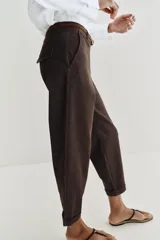 Pantalón chino de tiro bajo color marrón oscuro, con pernera recta y bajo con vuelta. Incluye un cinturón trenzado delgado de color marrón claro. Cuenta con bolsillos delanteros y cierre frontal con cremallera y botón.