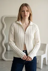 Sweater de punto acanalado color crema, con cuello alto y cierre frontal doble. Presenta mangas largas y diseño entallado.