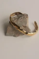 Brazalete rígido abierto de bronce con textura irregular.