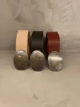 Cinto de cuero con hebilla ovalada de metal con diseño labrado. Disponible en color natural, marrón y bordó.