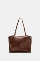 Bolso tipo mini shopper confeccionado en piel con acabado brillante. Presenta un diseño de doble compartimento con cierre de botón imantado y asa de hombro ajustable.