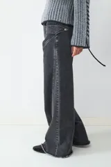 Jean wide leg de denim gris oscuro, con tiro medio, cierre de botón y cremallera. Presenta un diseño de pierna ancha con costuras decorativas en la parte delantera y ruedo deshilachado.