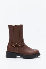 Bota tipo biker de caña media en cuero sintético negro, con panel elástico lateral, suela gruesa dentada y arnés decorativo con herraje metálico.