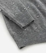 Suéter de punto color beige con cuello redondo, manga larga y aplicaciones de perlas distribuidas por toda la prenda. Presenta puños y ruedo acanalados.