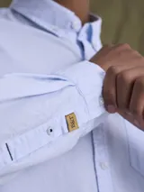 Camisa de manga larga confeccionada en tejido Oxford de algodón, con cuello abotonado (button-down) y bolsillo frontal en el pecho.