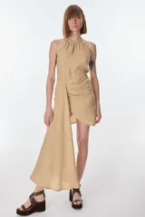 Vestido halter color beige, con cuello fruncido y drapeado asimétrico en la cintura que genera una cola larga en un lateral.