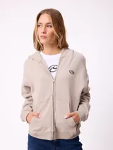 Canguro con cierre frontal de la marca Rusty, en color beige. Presenta capucha, bolsillos tipo canguro y logo bordado en el pecho.