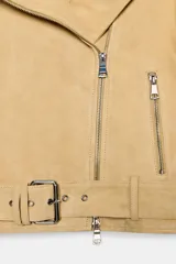 Chaqueta estilo biker de piel de ante 100% color beige, con cuello solapa, manga larga, bolsillos con cremalleras metálicas y bajo ajustable con hebilla. Cierre frontal con cremallera metálica.