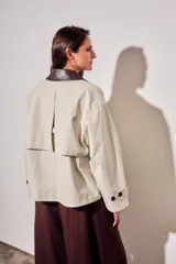Trench corto de corte oversize con estampado de cuadros finos en tonos beige y verde. Presenta cuello camisero en contraste de color marrón oscuro, cierre frontal con botones y mangas largas con detalle de trabas en los puños.
