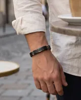 Pulsera para hombre con banda central de acero inoxidable grabada con diseño de guarda griega y laterales de cuerina negra texturizada.
