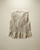 Chaleco de lana merino color crudo, con diseño artesanal que presenta apliques florales en relieve y terminación de flecos en el ruedo.