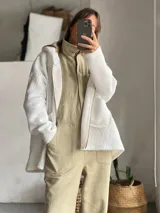 Campera de corderito blanco con capucha, de corte holgado y diseño largo. Presenta un aplique rectangular en la espalda con diseño geométrico de semicírculos en tonos verde y naranja con estampado floral pequeño.