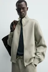 Sudadera de corte relajado confeccionada en tejido técnico interlock de algodón con elasticidad. Presenta cuello subido, cierre frontal con cremallera, manga larga con puños acanalados y bolsillos laterales ocultos en las costuras.