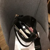 Cartera tipo morral en eco cuero con textura símil gamuza marrón, costuras blancas visibles y correa ajustable de lona.