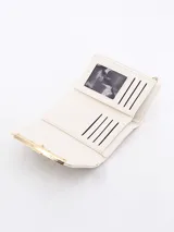 Billetera compacta color beige con solapa frontal y detalle de barra metálica dorada en el cierre.
