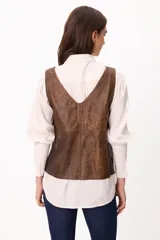 Chaleco de cuero gamuzado color marrón, con escote en V y cierre frontal mediante tiras para anudar.