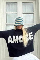 Sweater de punto negro con cuello redondo y mangas largas, presenta la palabra 'AMORE' estampada en letras grandes de color blanco en el frente.