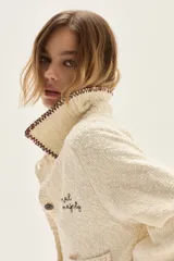 Cardigan de punto color crudo con textura, cuello camisero con borde en contraste, mangas largas con puños acampanados y detalle de bordado floral en la espalda.