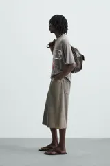 Camiseta gris de punto con efecto lavado y roturas, corte "boxy fit", cuello redondo y manga corta. Presenta un estampado frontal en blanco y rojo con diseño abstracto.