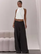Top blanco con diseño halter, cuello alto y espalda descubierta. Presenta un frente cruzado con pliegues, bajo elástico y lazo de ajuste en la espalda.