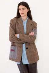 Blazer de corte sastrero confeccionado en paño con estampado de cuadros escoceses. Presenta parches decorativos en las mangas y espalda, bordados en el bolsillo y manga, y cierre frontal con botones.