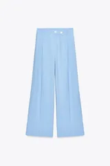 Pantalón celeste de tiro alto con pinzas delanteras, bolsillos laterales y falsos bolsillos traseros. Pierna ancha y cierre frontal con cremallera y botones.