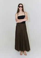 Falda larga color marrón oscuro, con diseño evasé, tiro medio y detalle cruzado tipo pañuelo con cierre de nudo en la cintura.