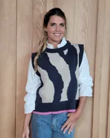 Chaleco tejido de punto con diseño abstracto bicolor en tonos gris oscuro y beige. Presenta cuello redondo, sisas amplias y un detalle de franja en color rosa en el ruedo inferior.