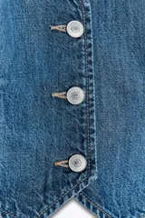 Chaleco de denim azul con cuello halter y escote pico. Presenta falsos bolsillos de vivo en el delantero y cierre frontal con botones metálicos.