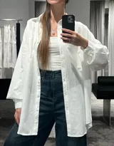 Camisa de corte oversize color marrón, con cuello clásico, cierre frontal de botones y mangas largas con puños ajustables. Presenta un diseño de hombros caídos y un bolsillo frontal en el pecho.