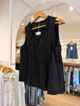 Blusa sin mangas de color negro, con delicadas tablitas frontales, cierre de botones al tono y cuello redondo decorado con un sutil volado fruncido.
