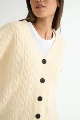 Cardigan de punto con diseño de trenzas, color beige, con escote en V, cierre frontal de botones negros y mangas largas con puños acanalados.