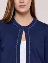 Cardigan corto azul marino de punto, con silueta entallada y largo a la cintura. Cuenta con un ribete decorativo que recorre el cuello redondo y la abertura frontal, integrando una cadena dorada en contraste. Posee bolsillos delanteros simulados y mangas largas.
