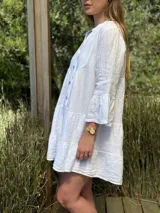 Vestido amplio de lino color verde lima, con cuello mao y abertura frontal con botones de coco. Presenta un diseño con canesú fruncido y volados en los puños de las mangas largas.