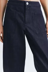 Pantalón de jean azul oscuro de tiro medio, con corte holgado y diseño de pierna ancha. Presenta cintura elástica en la parte posterior, cierre frontal con cremallera y botón metálico, y bolsillos de plastrón en el delantero.