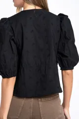 Blusa negra de algodón con diseño de broderie, mangas tres cuartos abullonadas, cierre frontal con botones y detalle de cordón ajustable en la cintura.