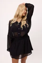 Vestido corto de chiffon color verde lima, con transparencia, cuello camisero, botones frontales y elástico en la cintura. Las mangas son largas y abullonadas con puños elásticos.