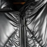 Campera puffer plateada con cuello alto, cierre frontal negro, bolsillos laterales y elástico interno para mejor ajuste.