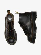 Botas Dr. Martens modelo Church Quad de cuero negro, con plataforma gruesa acanalada, costuras amarillas contrastantes y cordones negros.