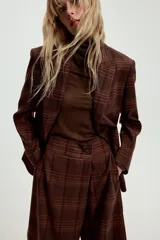 Blazer Zara de cuello solapa y manga larga, con estampado de cuadros en tonos marrones y rojizos. Presenta cierre frontal con dos botones y bolsillos delanteros con solapa.