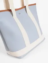 Bolso tipo tote bag de tamaño medio, color negro, con franjas verticales y base en color celeste. Posee asas cortas de cinta tejida y refuerzos de poliuretano color marrón claro.