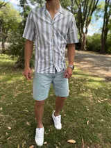 Camisa de manga corta con diseño de rayas verticales en tonos gris y blanco, cuello abierto estilo cubano y cierre frontal con botones de madera.