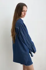 Camisa de jean azul, de corte holgado y manga larga, con cuello camisero y cierre frontal de botones oscuros.